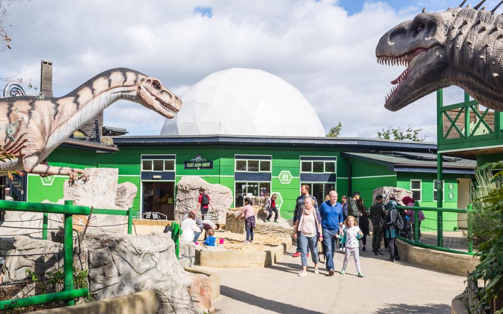 Entrance of Gulliver's Dinosaur & Farm Park with people and large dinosaur replicas.