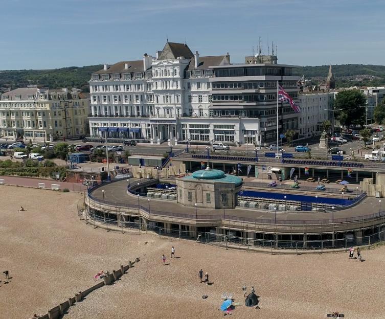 View of a sandy beach and a boardwalk leading up to a large white building in a town.