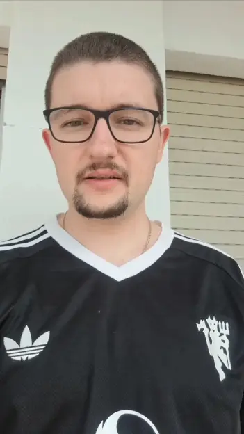 Man wearing glasses and a black Adidas shirt with a Manchester United logo.