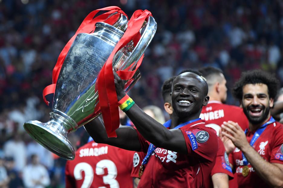 Sadio Mané holding up the UEFA Champions League trophy, with Mohamed Salah smiling behind him.
