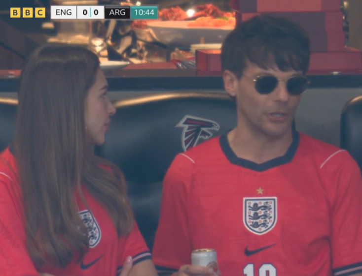 A man and a woman in red jerseys watching a soccer game.