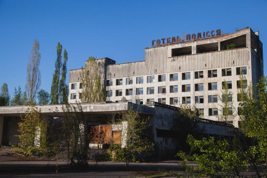 The Polissya Hotel in Pripyat, an abandoned concrete building with broken windows and trees growing around it.