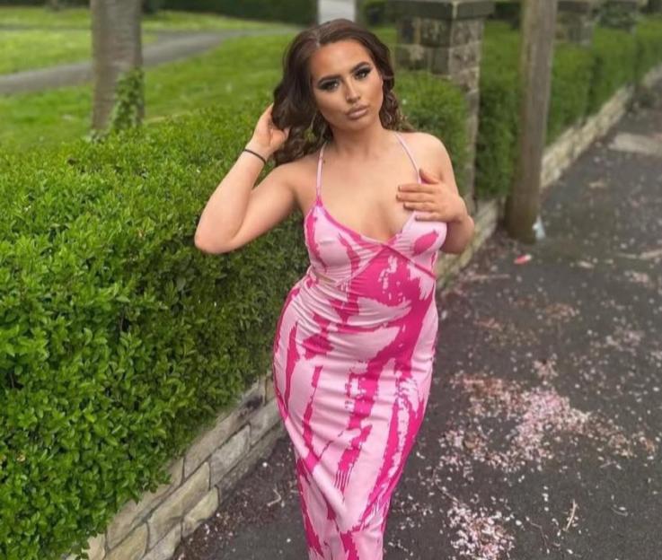 A young woman wearing a pink and white patterned dress poses outside.
