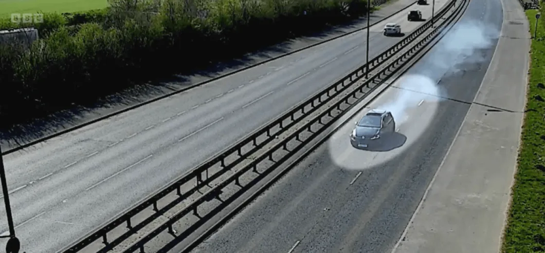 A black car releasing a large cloud of smoke from its tires on a highway.