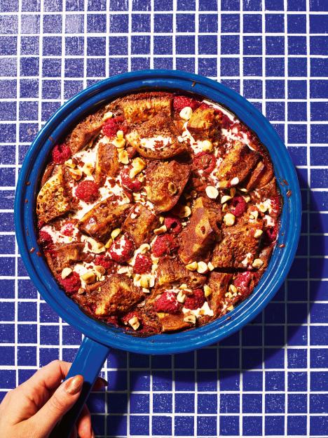 Crumpet pudding with raspberries, nuts, and cream in a blue pan.