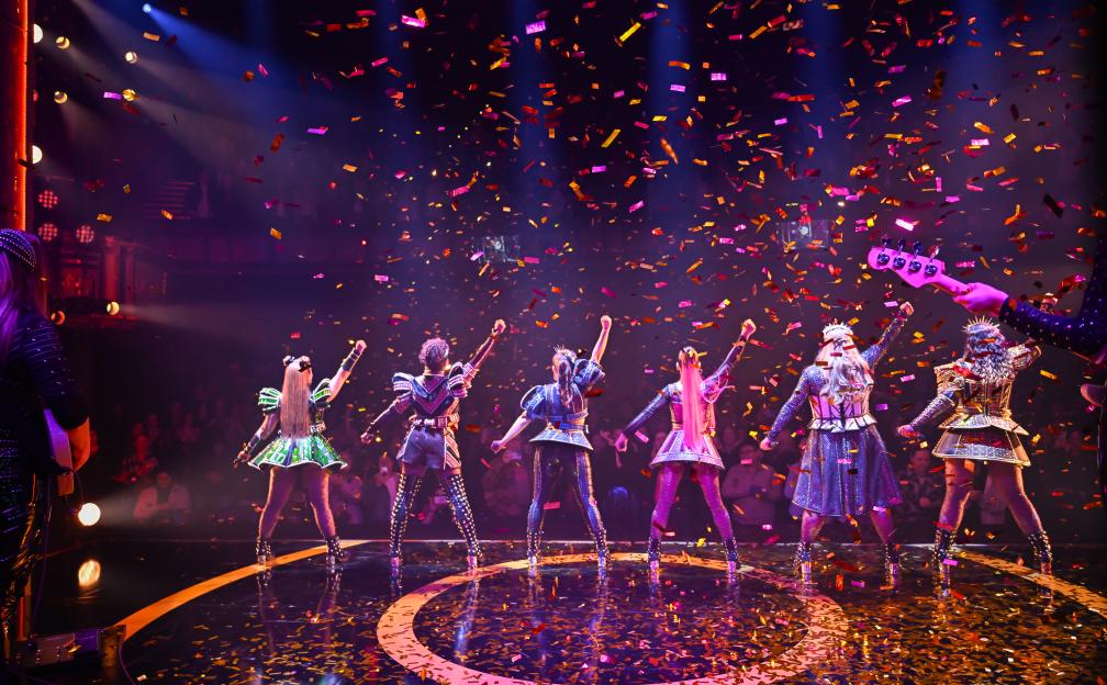 The cast of SIX The Musical on stage, viewed from the back, with confetti falling.