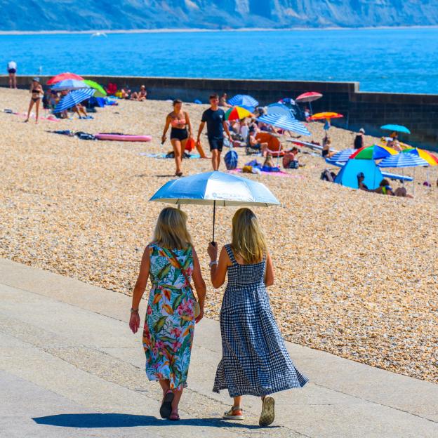 Two women walking along a beach in Lyme Regis, Dorset, one holding a silver umbrella.
