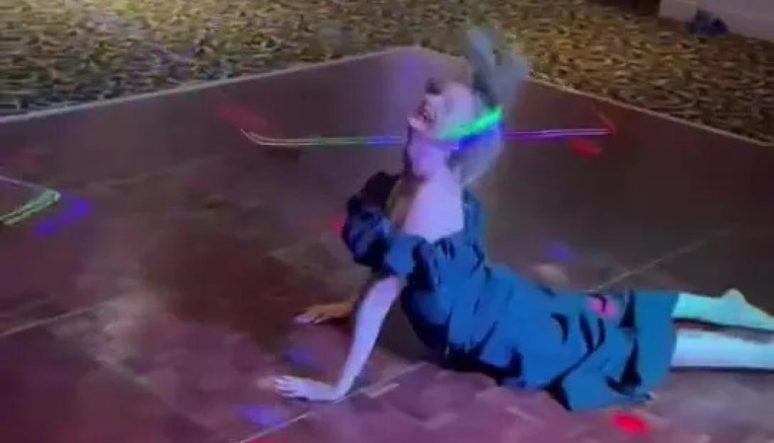 Woman in a black dress lying on a dance floor at a wedding, with colorful lights on the floor and her hair in motion.