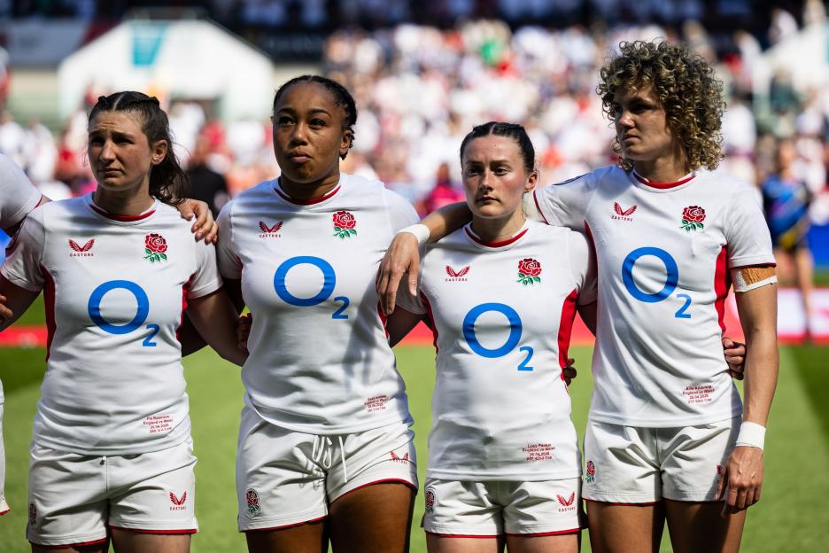 Four England Women's rugby players, wearing white jerseys with red roses, standing with arms linked.