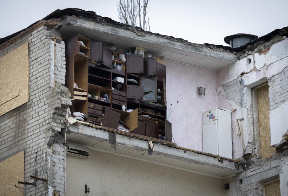 The interior of a damaged apartment building in Ukraine shows a refrigerator and broken cabinets, with the outer wall missing.