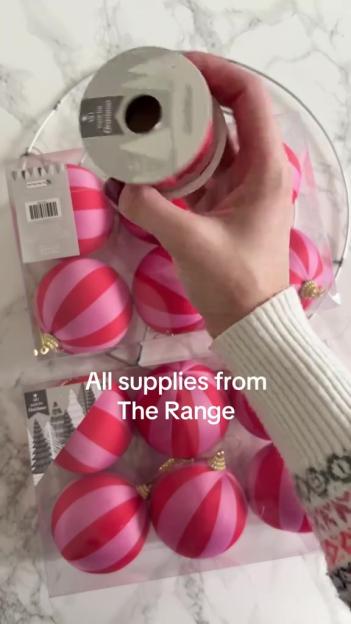 Hand holding a spool of red ribbon and packaged pink and red striped ornaments from The Range.