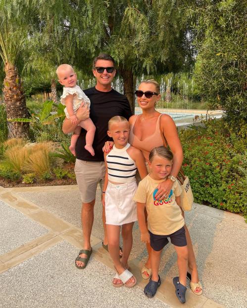 Billie Faiers, her partner, and three children smiling in front of green foliage and a water feature.