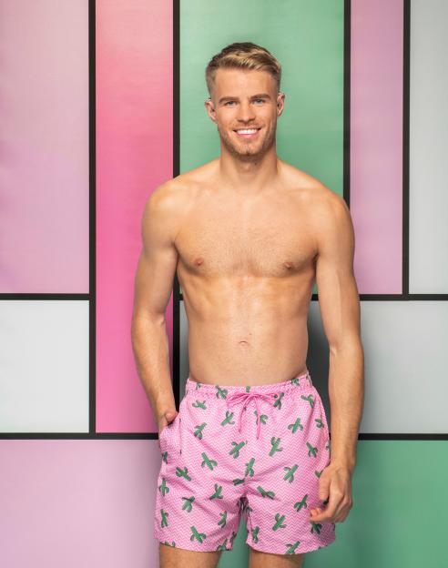 Sam from Love Island Series 13, posing shirtless in pink swim trunks with green cactus patterns.