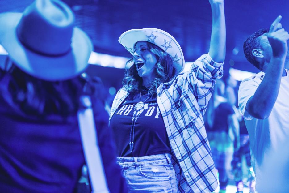 A woman in a cowboy hat and plaid shirt sings with her arm raised.