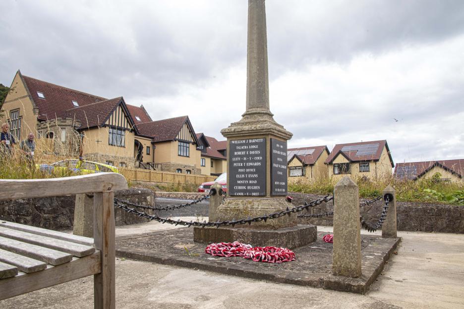 War memorial with names inscribed on two plaques, with wreaths of red poppies at its base, in the town of Gronant on the North Wales coast.