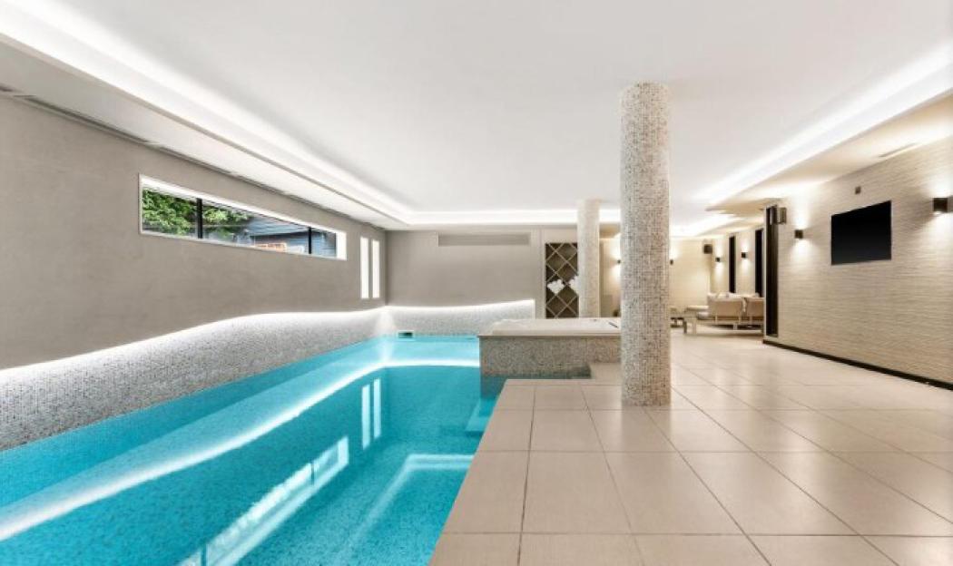 Indoor swimming pool with light blue water and white tiled walls.