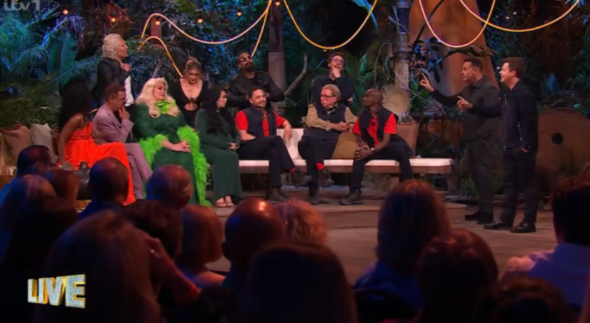 A group of people, including two hosts, on a TV set with an audience in the foreground.