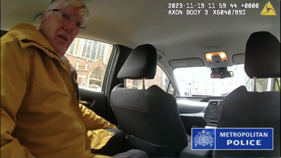 John Grant in the backseat of a police vehicle, with the Metropolitan Police logo visible.