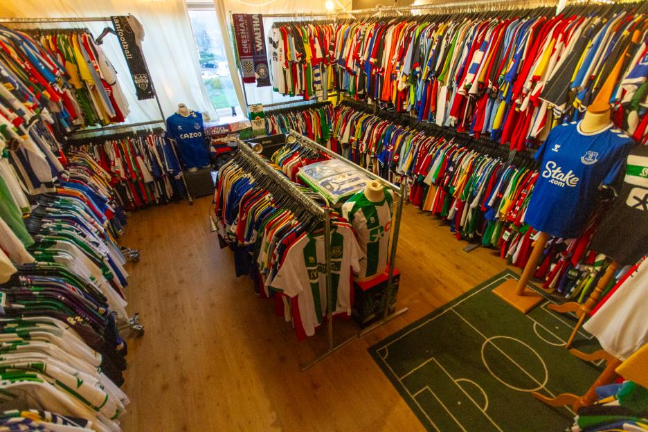 A room filled with racks of colorful soccer jerseys and a green rug designed like a soccer field.