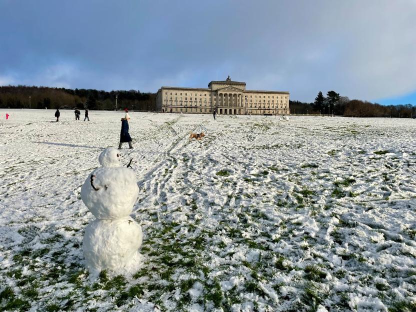 Wintry conditions on the Stormont estate in east Belfast with people and a snowman on a snow-covered field.