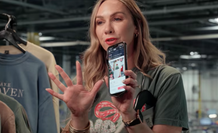 A woman presenting a mobile phone with an e-commerce website displaying clothing items.