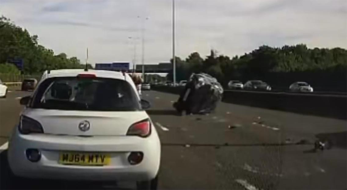 Dash cam footage of a car rolling twice on the M25 motorway, with debris on the road and other cars in the background.