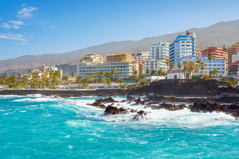 The coastline of Puerto de la Cruz in Tenerife, Canary Islands, Spain, with hotels, palm trees, and the Atlantic Ocean.