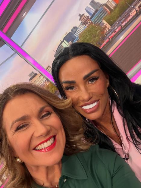 Katie Price with long dark hair, wearing a pink shirt, and Susanna Reid with blonde hair, wearing a green shirt, smiling and embracing for a selfie.