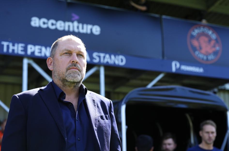 A man in a dark blue jacket and shirt looking forward at the Peninsula Stadium.
