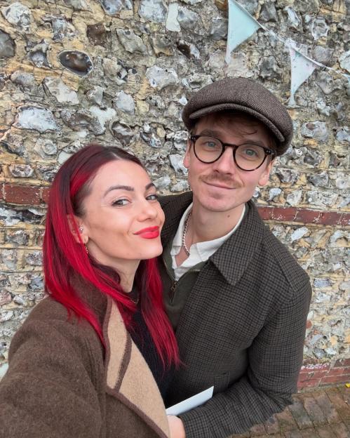 Strictly’s Dianne Buswell and boyfriend Joe Sugg smiling in front of a stone wall.