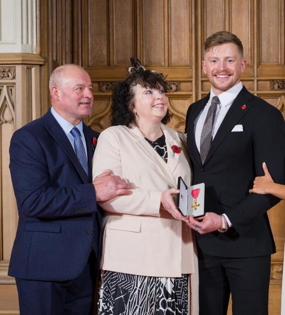 Adam Peaty with his family, holding his OBE medal.