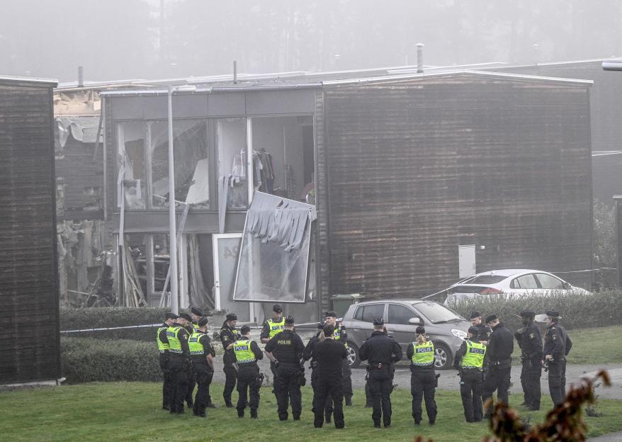 Policemen stand in front of a building damaged by a powerful explosion.