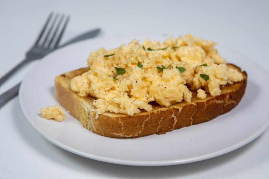 Scrambled eggs on toast with pepper and parsley, on a white plate with cutlery on the side.