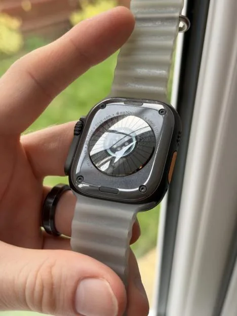 Close-up of the back of an Apple Watch Ultra in a black case with a light-colored ocean band.