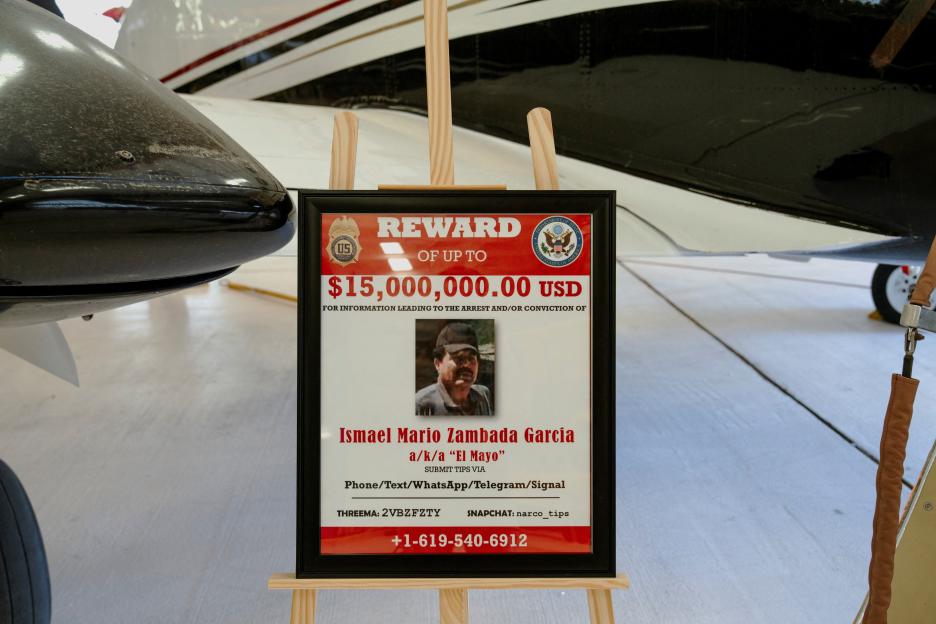 A reward sign for Ismael "El Mayo" Zambada is displayed next to a Beechcraft King Air aircraft.