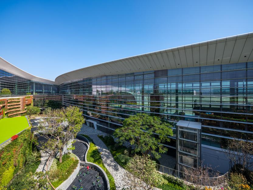A modern airport building with a curved glass facade and surrounding landscaped gardens with green walls and walkways.
