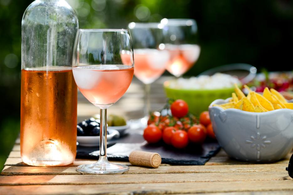 Outdoor summer brunch table with a bottle and glasses of rosé wine, fresh vegetables, and snacks.