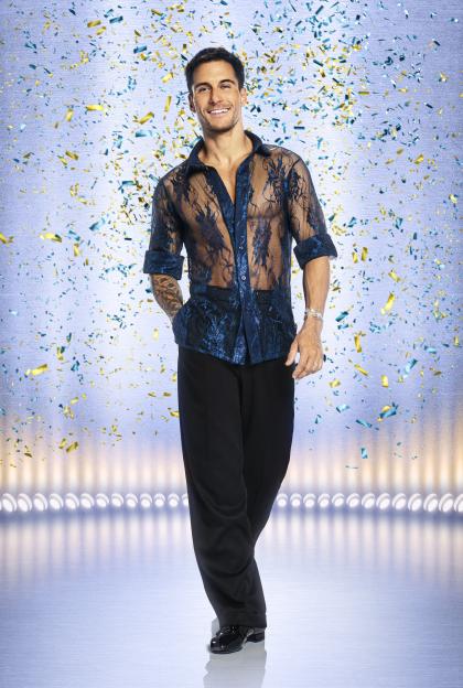 Gorka Marquez, a smiling man with dark hair, wears a sheer blue lace shirt and black pants, with confetti falling around him on a stage.