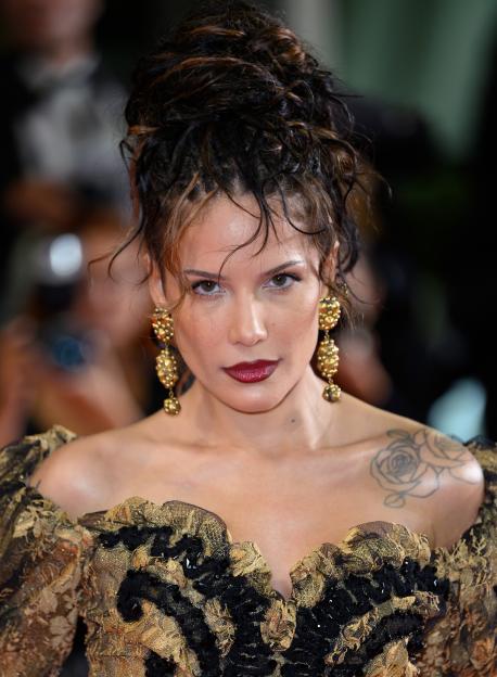 Halsey wearing a black and gold Vivienne Westwood dress with matching gold drop earrings and red lipstick.