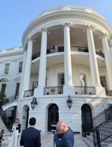The back of the White House with people filming in front of it.