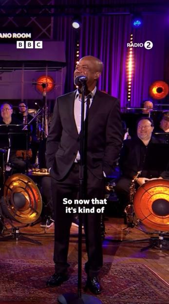 Darius Rucker singing into a microphone on stage with a band in the background.