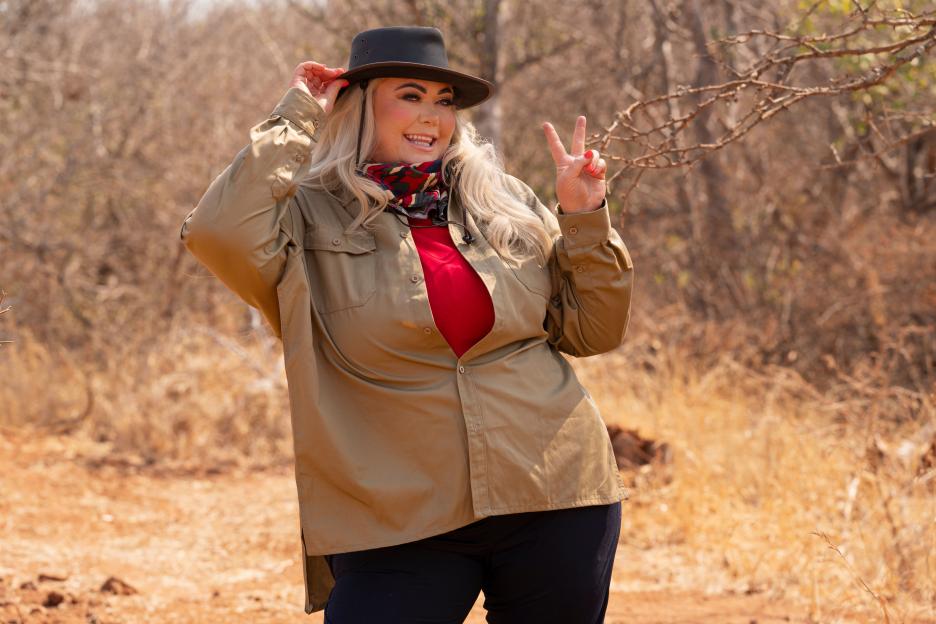 Gemma Collins, a media personality and businesswoman, posing in a khaki shirt, red top, and a hat, making a peace sign with her left hand.