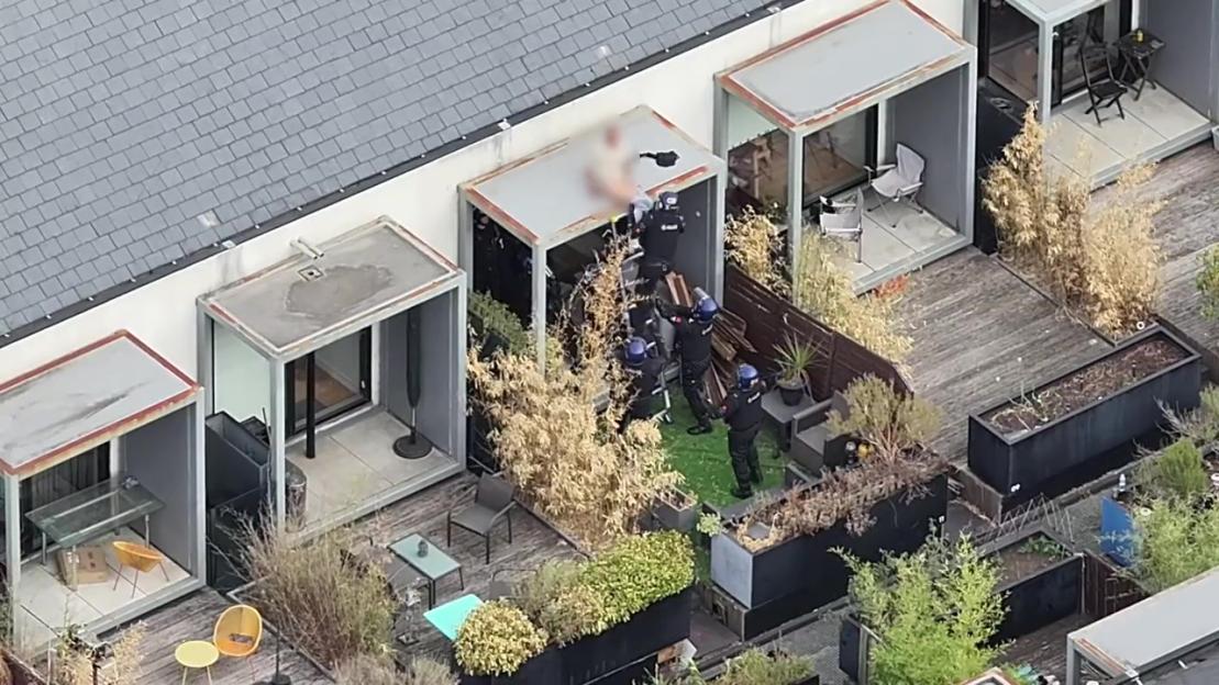Police officers arresting a man on a rooftop balcony.