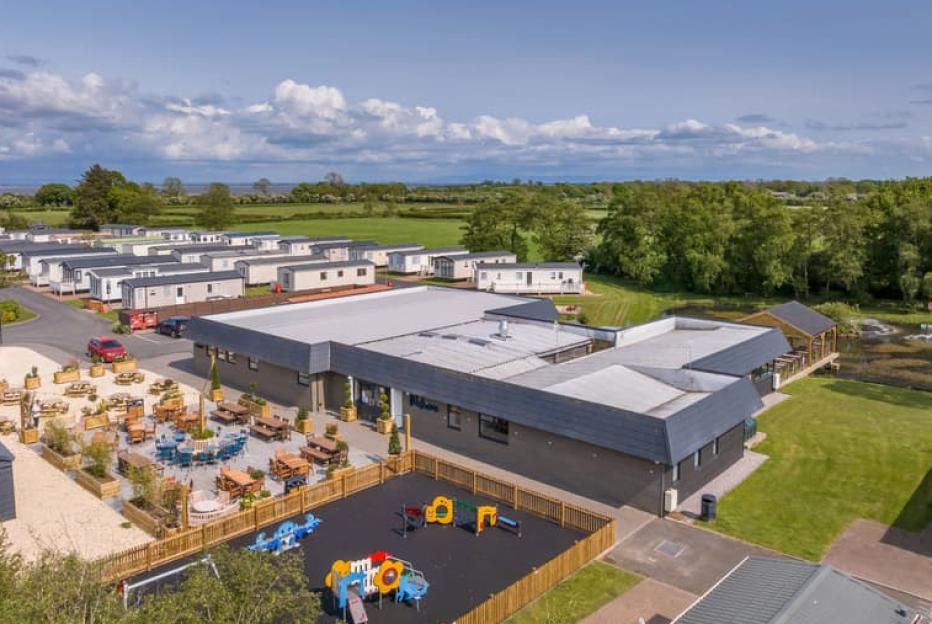 Aerial view of Glendale Holiday Park in Cumbria, showing the main building, an outdoor seating area, a playground, and numerous mobile homes.