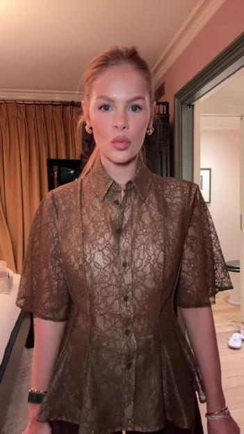 A woman in a brown lace peplum top, gold hoop earrings, and a gold watch and bracelets.