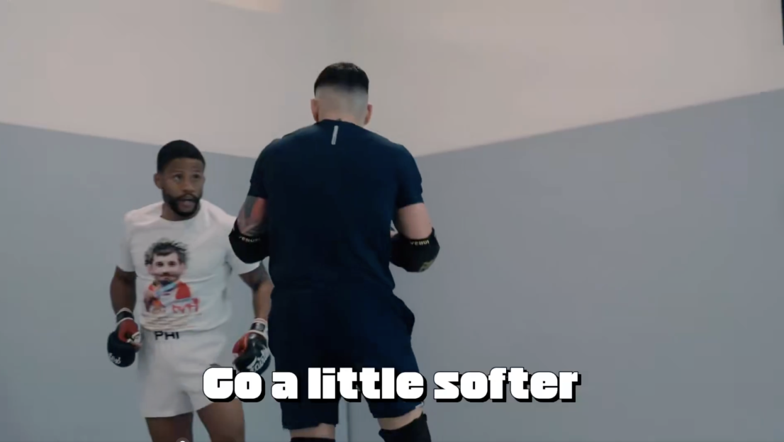 Two men in a boxing ring, with one wearing a white shirt and the other in a black shirt, both with boxing gloves.