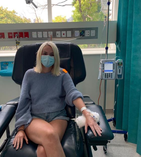 Charlotte Rutherford, age 32, sitting in a hospital chair with an IV in her arm.