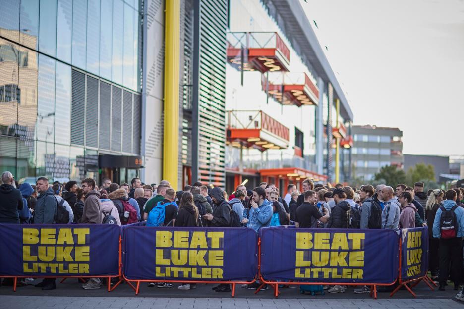 A large crowd of people standing in line behind "Beat Luke Littler" banners for auditions.