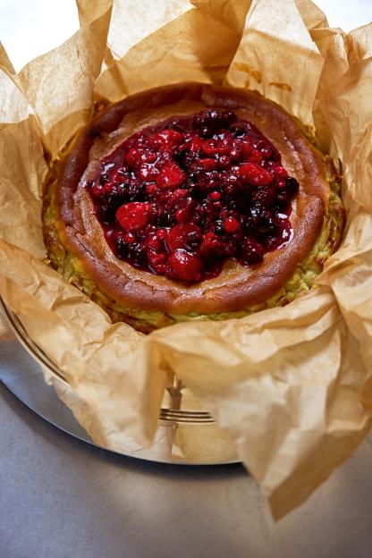 Baked Basque cheesecake topped with berry compote, in a round baking dish lined with crumpled parchment paper.