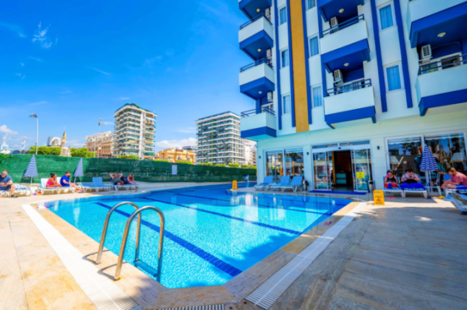 A swimming pool area with blue and white striped lounge chairs and umbrellas, and tall buildings in the background.